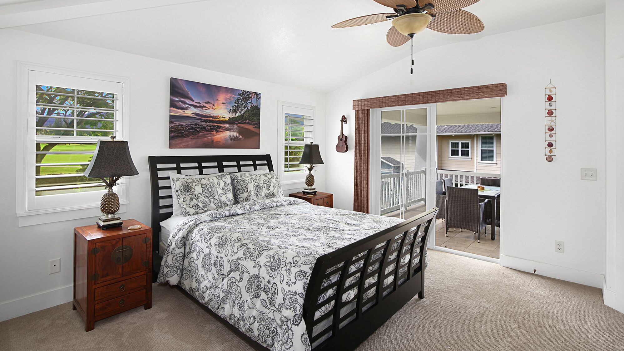 Une chambre à coucher comprenant un lit, deux tables de chevet, un ventilateur de plafond, une fenêtre avec des stores et une vue sur un balcon.