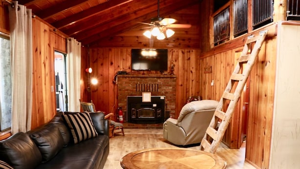 A cozy cabin interior with a leather sofa, a round wooden table, a fireplace, and a ladder. -  Holiday Hide Away  (Payson)