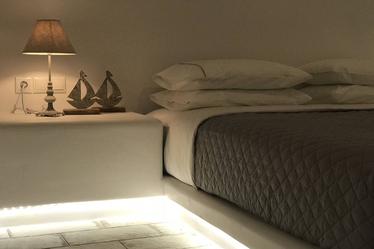 Uma cama bem arrumada com cobertura acolchoada, abajur e objetos decorativos na mesinha de cabeceira.