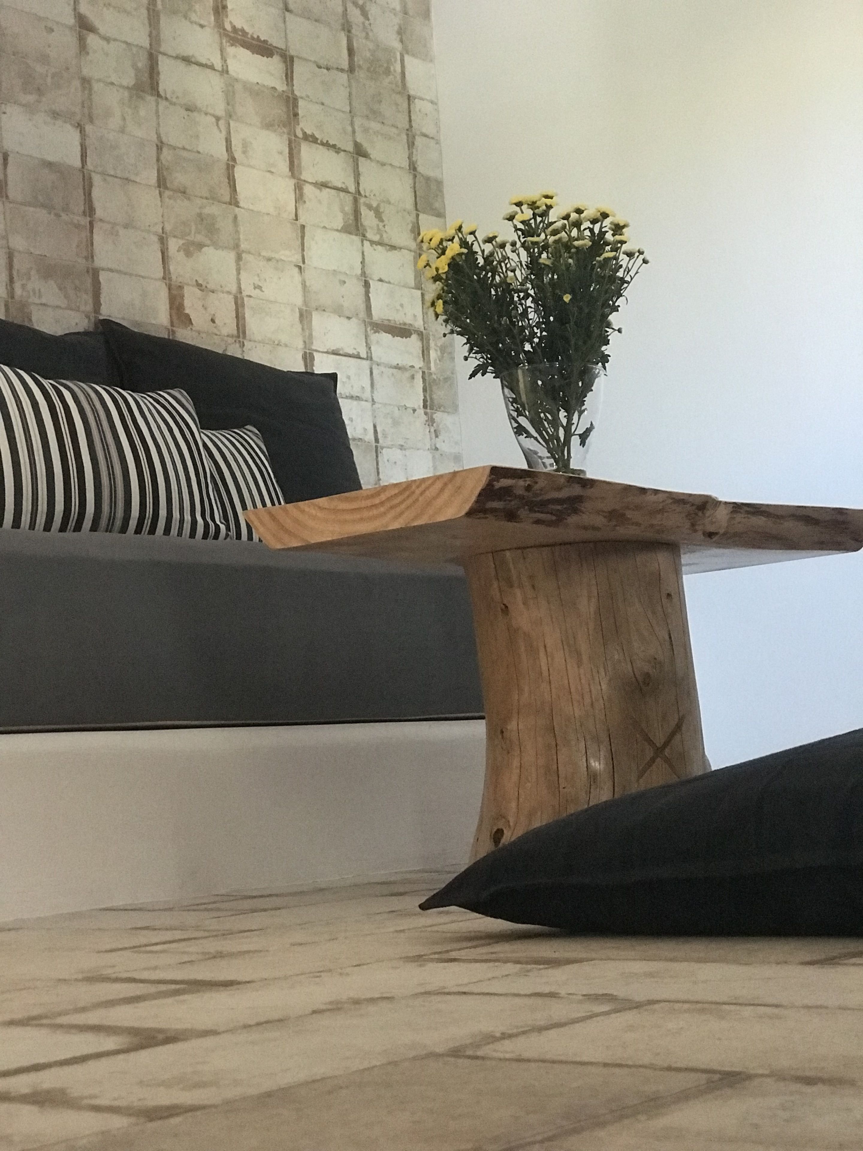 Un salón moderno con un sofá gris, cojines negros y una mesa de centro de madera con un jarrón de flores amarillas.