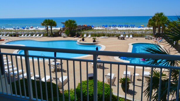 A pool area with lounge chairs and umbrellas, a beach in the background, and a clear sky. - 2000sqft Beachfront Beauty on Perdido Key.  (Pensacola)