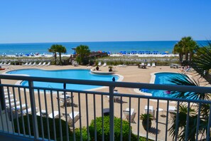 Ein Poolbereich mit Liegestühlen und Sonnenschirmen, im Hintergrund ein Strand und ein klarer Himmel.
