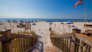 A wooden staircase leading to a sandy beach with blue umbrellas and a flag. - 2000sqft Beachfront Beauty on Perdido Key.  (Pensacola)