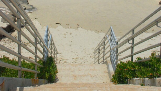 A beach with a staircase leading down to the shore, surrounded by metal railings and greenery. - Beachcombers Hideaway, Dog Friendly, Enclosed Patio, 1 Block to Beach (La Jolla)