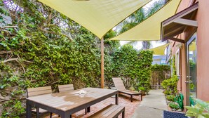 A patio with a wooden table and benches, surrounded by lush greenery and a yellow canopy. - Beachcombers Hideaway, Dog Friendly, Enclosed Patio, 1 Block to Beach (La Jolla)