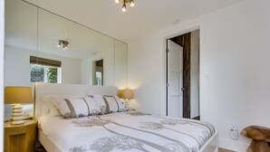 A bedroom with a large bed, bedside lamps, a mirror, and a wooden stool. - Beachcombers Hideaway, Dog Friendly, Enclosed Patio, 1 Block to Beach (La Jolla)