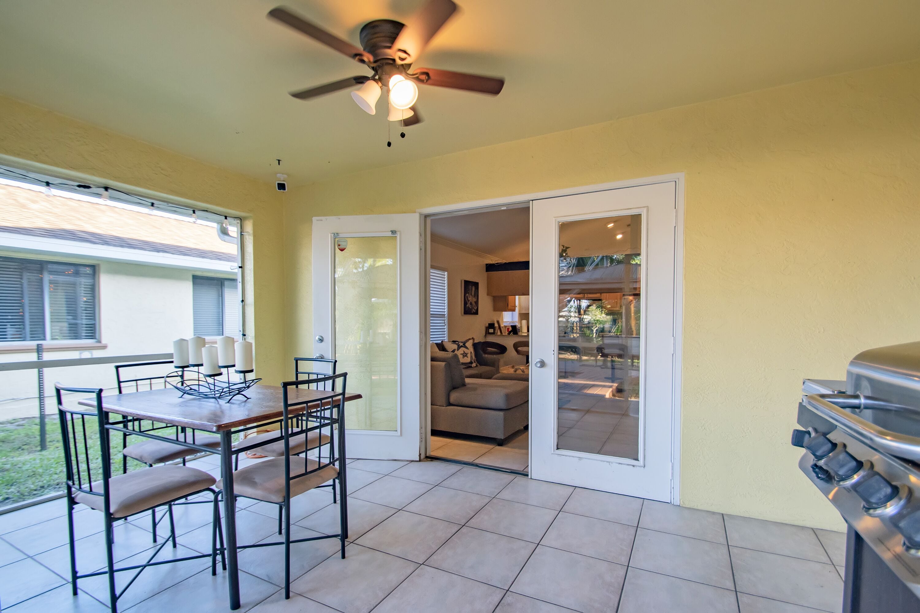 An outdoor patio area with a dining table, chairs, a ceiling fan, and a grill.