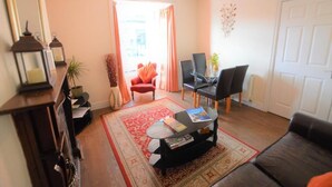 Una sala de estar con un sofá, una mesa de centro, una silla, una mesita con una lámpara y una puerta.