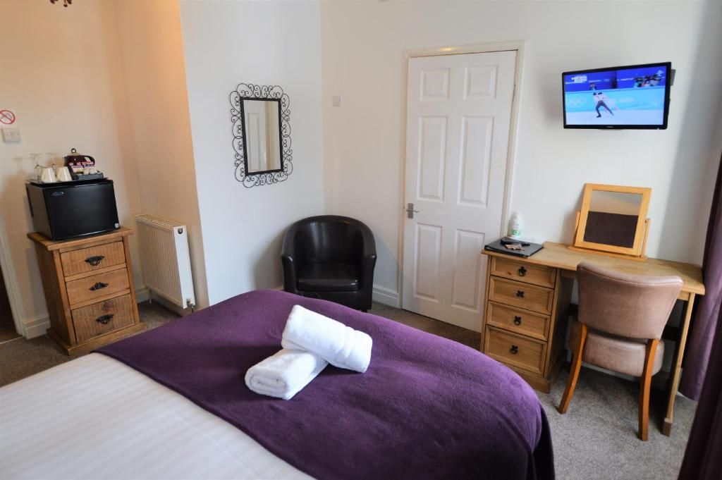 Quarto de hotel com cama, escrivaninha, cadeira, televisão e porta.