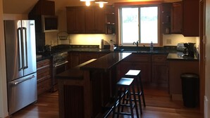 A spacious kitchen with wooden cabinets, a stainless steel refrigerator, a microwave, and a large island with bar stools. - Stage Road Estate private studio apartment. (Columbia Falls)