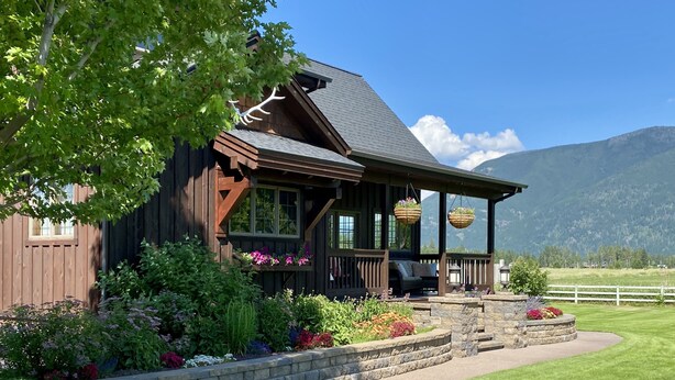 A wooden cabin with a porch, stone steps, and hanging flower baskets. - Stage Road Estate private studio apartment. (Columbia Falls)
