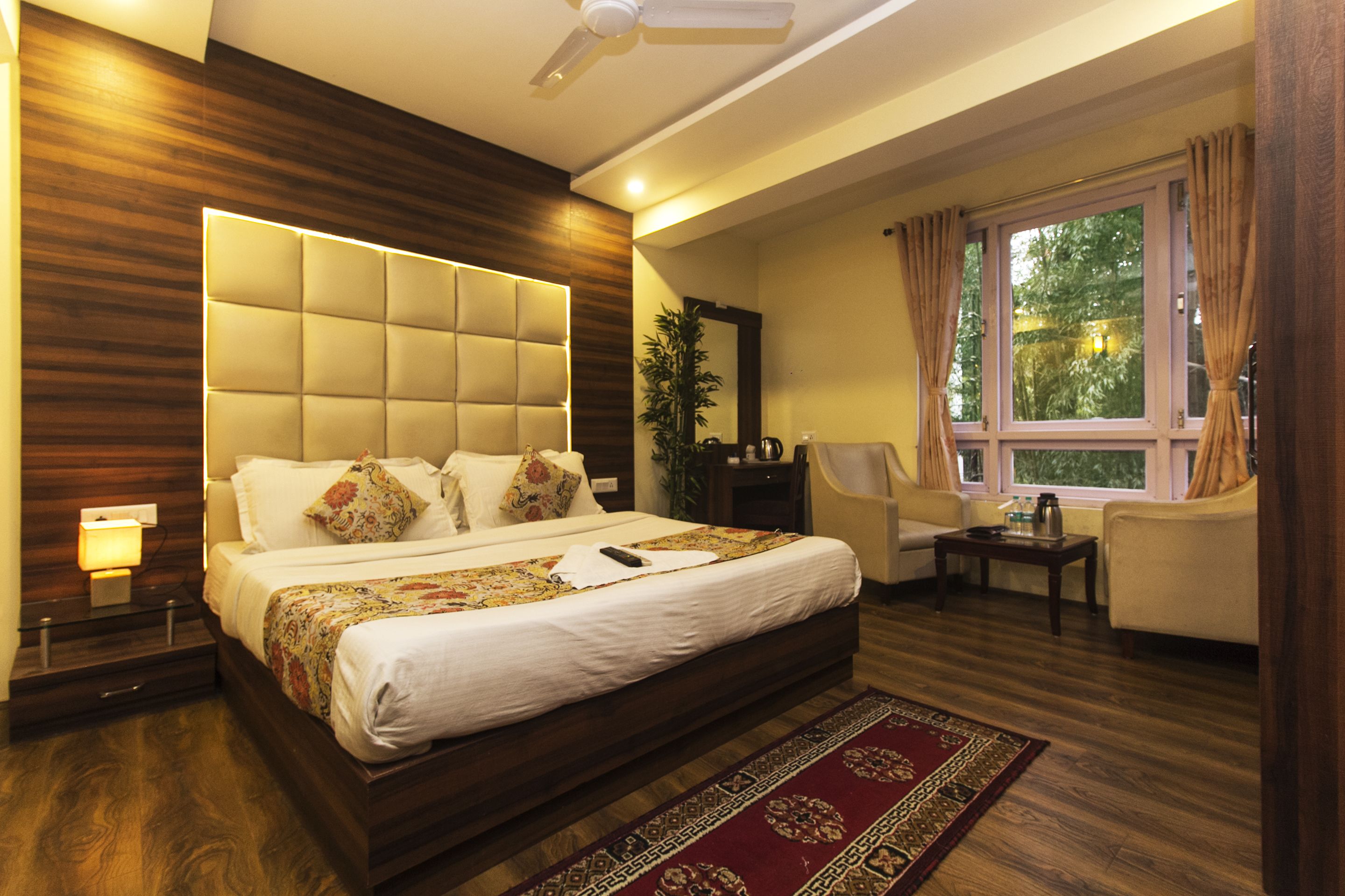 A modern bedroom with a large bed, a ceiling fan, a window with curtains, and a small table with a lamp.
