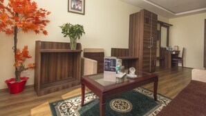 Un salon avec une table basse en bois, une plante en pot rouge, une plante en pot verte, un tableau encadré au mur et un meuble en bois.