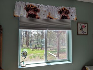 Ein Fenster mit Blick auf einen umzäunten Außenbereich, eine Zierblume und ein gerahmtes Bild an der Wand.
