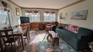 Una sala acogedora con una mesa de comedor de madera, un sofá verde y un televisor.