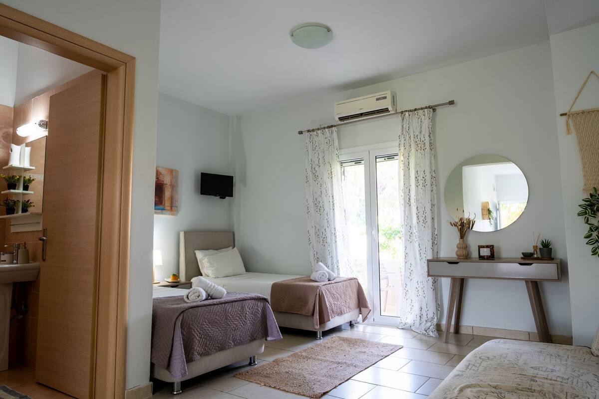 A bedroom with two beds, a TV, a mirror, and a bathroom visible through an open door.