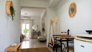A cozy living room with a wooden table, a sofa, and a dining area with chairs. There is a mirror on the wall and a plant hanging on the wall. - Tesys Studios & Apartments (Zakynthos)