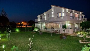 A two-story house with a well-maintained lawn, outdoor seating, and a thatched roof structure. - Tesys Studios & Apartments (Zakynthos)