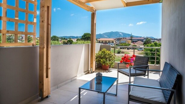 A balcony with a view of a town and mountains, featuring a table, chairs, and potted plants. - Tesys Studios & Apartments (Zakynthos)