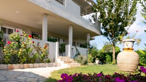 A modern building with a stone pathway leading to a white entrance, surrounded by lush greenery and vibrant flowers. - Tesys Studios & Apartments (Zakynthos)