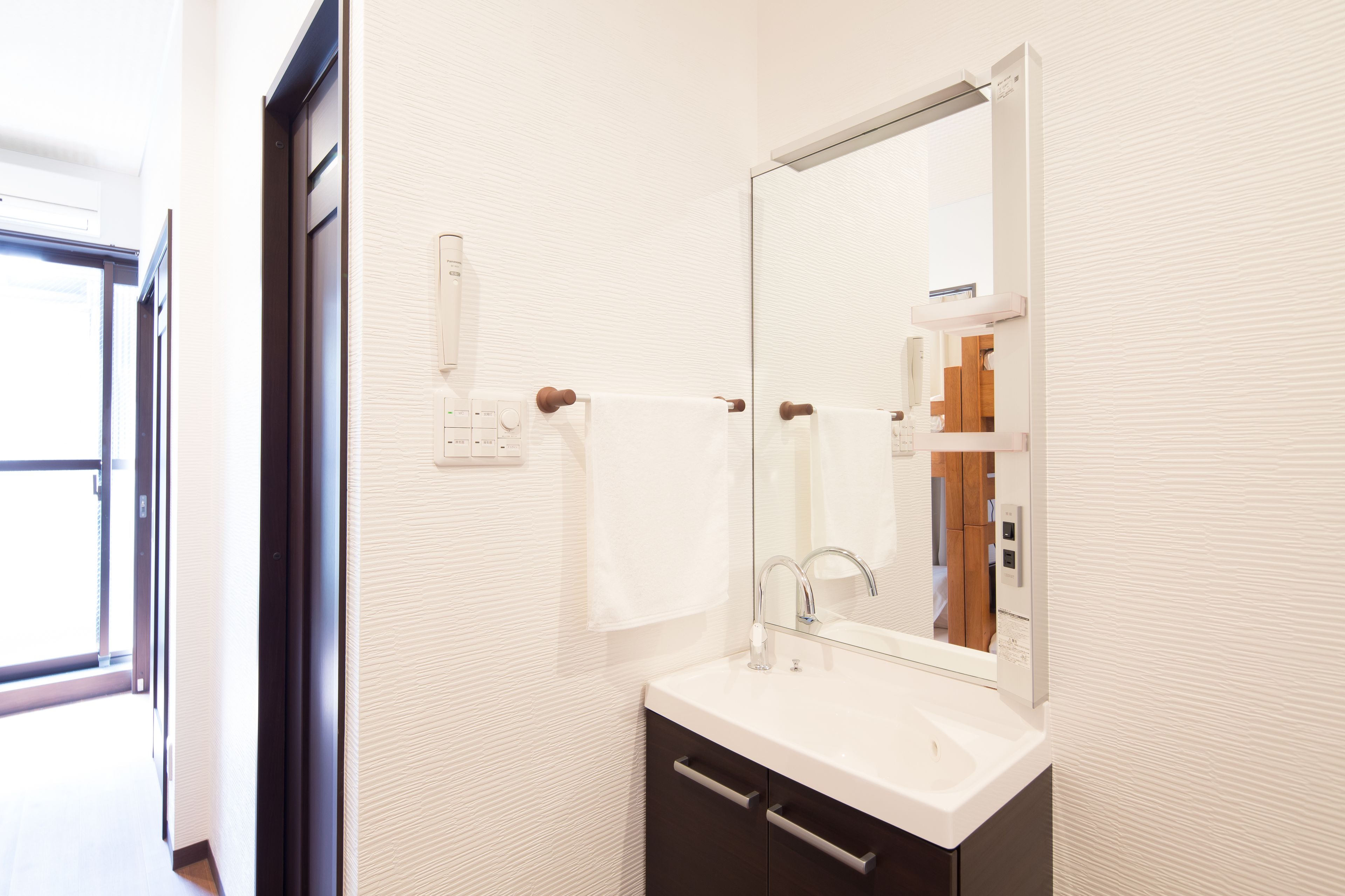 A modern bathroom with a white sink, a large mirror, and a towel rack.