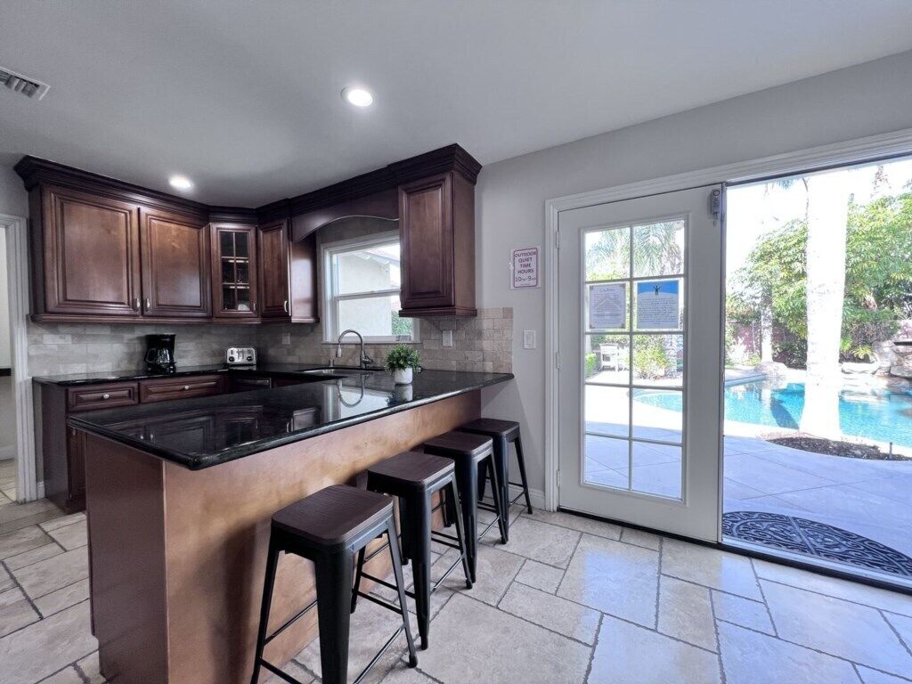 A kitchen with dark wood cabinets, a black countertop, and a large island with bar stools.