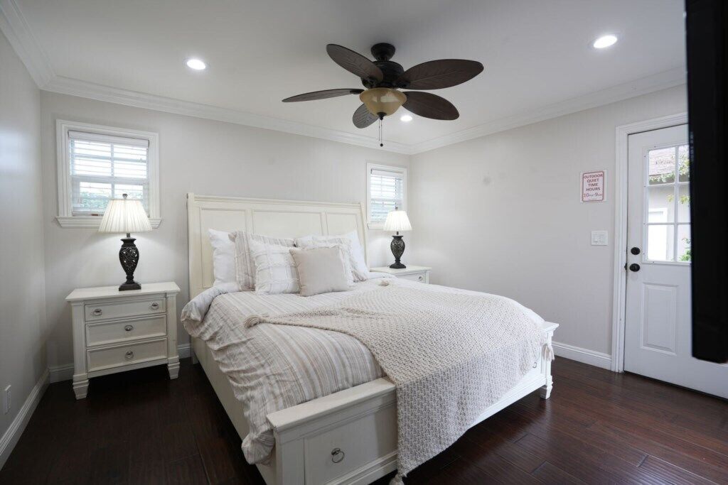 A bedroom with a bed, two bedside tables, a ceiling fan, and a door with a sign.