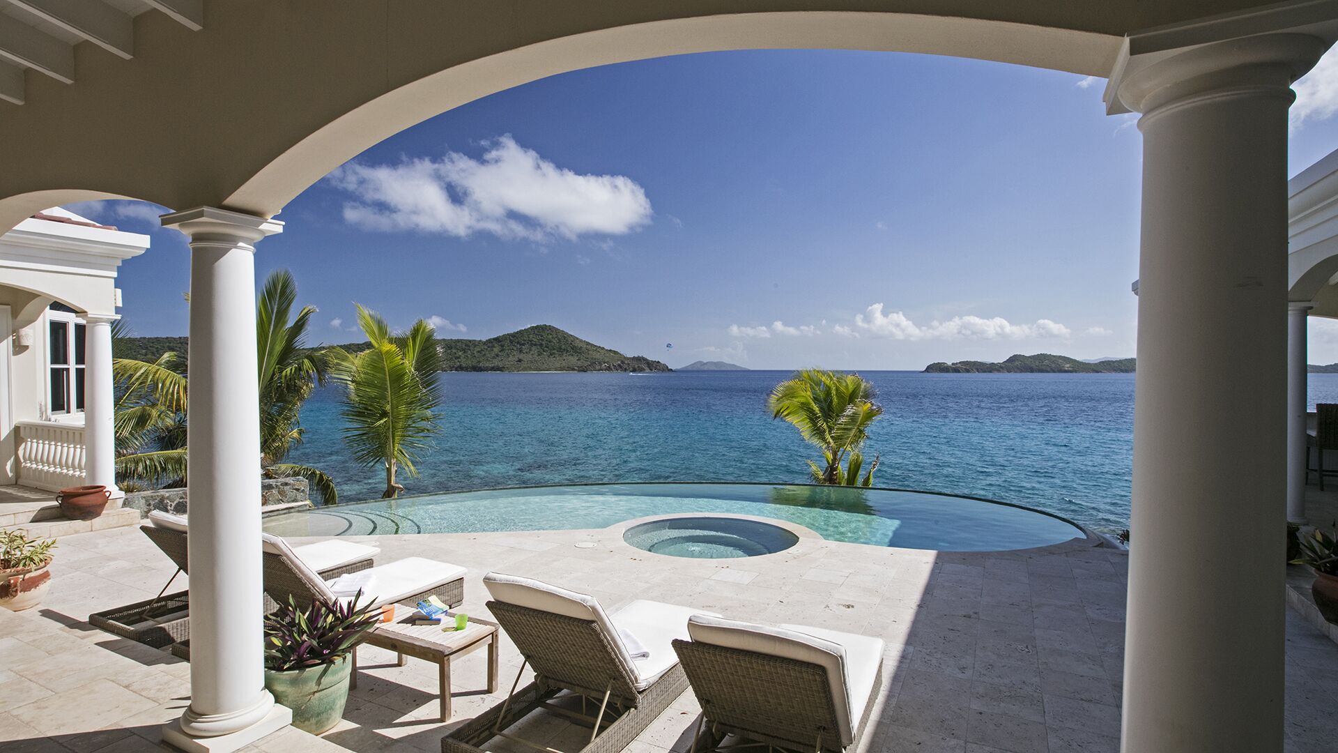 A pool area with a view of the sea, lounge chairs, and a pergola structure.