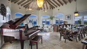Een ruime woonkamer met een vleugelpiano, een eettafel en uitzicht op de oceaan.