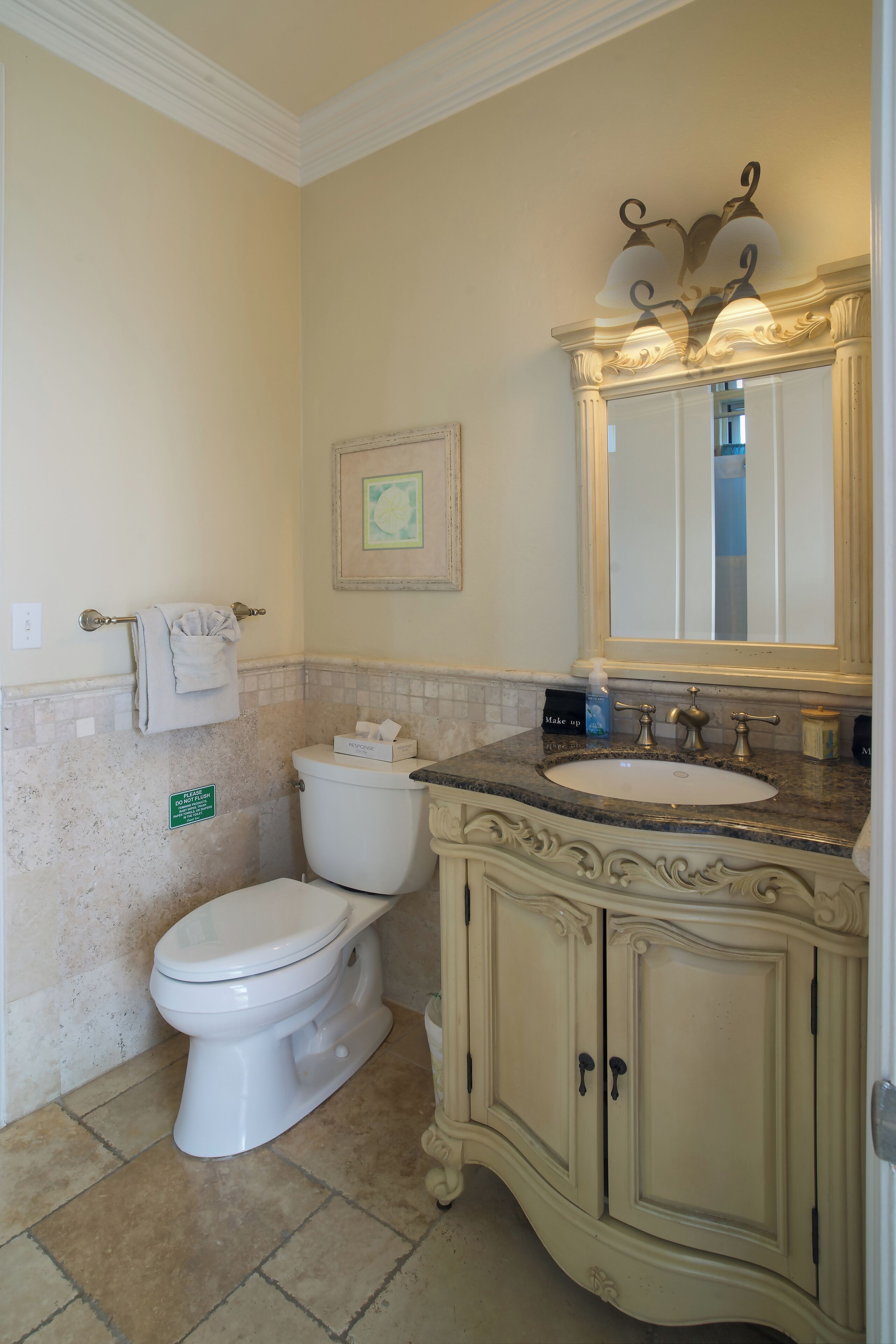 A bathroom with a toilet, sink, vanity, and a framed picture on the wall.