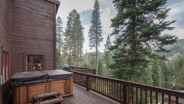 Une terrasse en bois avec un jacuzzi et un banc, donnant sur une zone boisée.