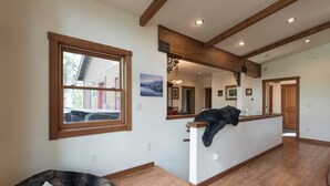 Un vaste espace de vie doté d’un plafond en bois, d’une grande fenêtre et d’un chat noir posé sur un comptoir.