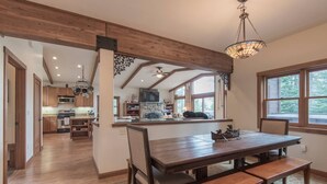 Une cuisine spacieuse avec des poutres en bois, un coin repas avec une grande table et des bancs, et une vue par la fenêtre.