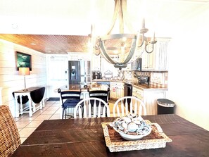 A dining area with a wooden table, white chairs, a chandelier, and a bowl of seafood on the table. - 1st Floor Amelia South's Oceanfront Crown Jewel   (Fernandina Beach)