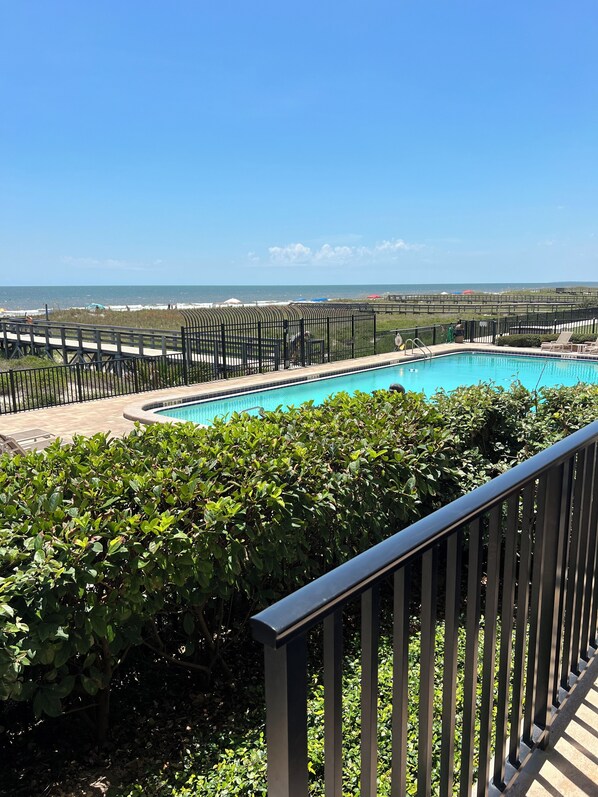 A swimming pool with a view of the ocean, surrounded by greenery and a wooden deck.
