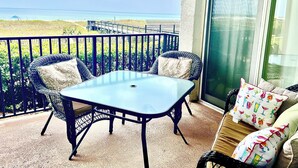 Un balcón con mesa y sillas, vista a la playa y una puerta corrediza de vidrio.