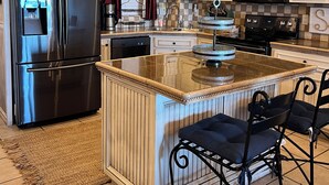 Una cocina moderna con un refrigerador de acero inoxidable, un microondas y una estufa. Cuenta con techo de madera y una isla grande con pileta.