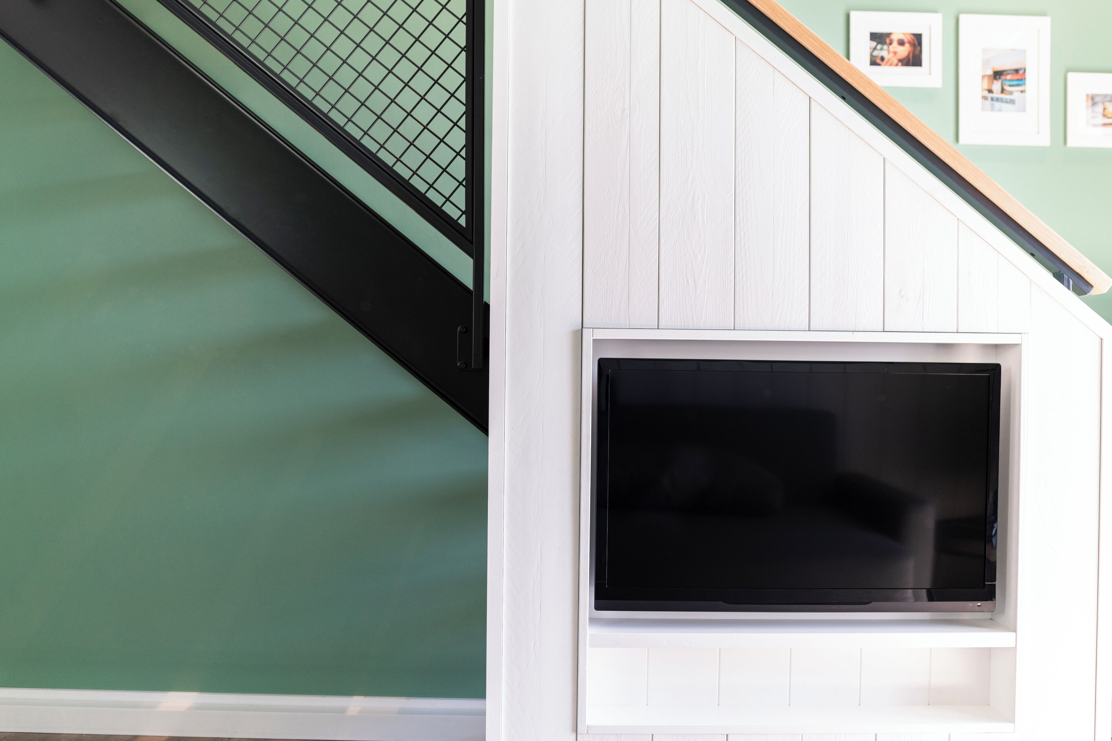A modern interior with a staircase, a flat-screen TV mounted on a white wall, and a green wall in the background.