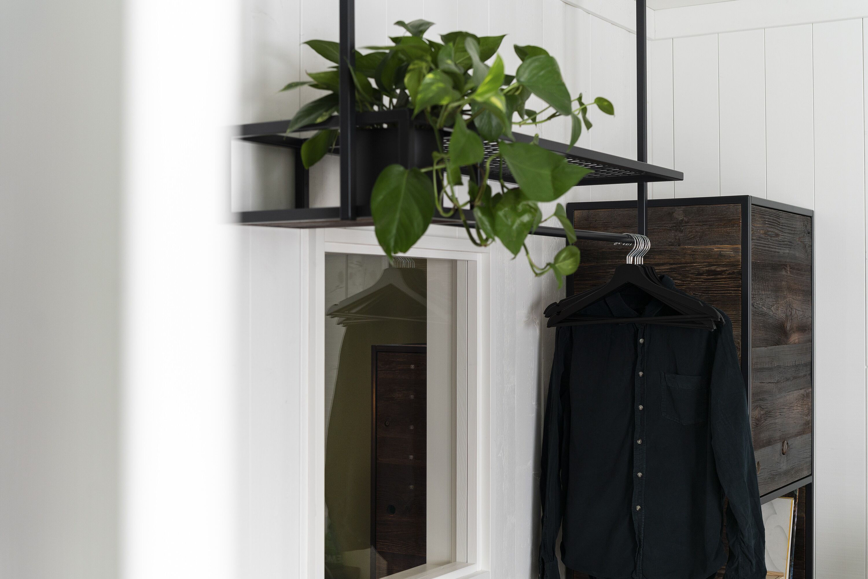 A room with a wooden cabinet, a black coat hanging, and a potted plant on a shelf.