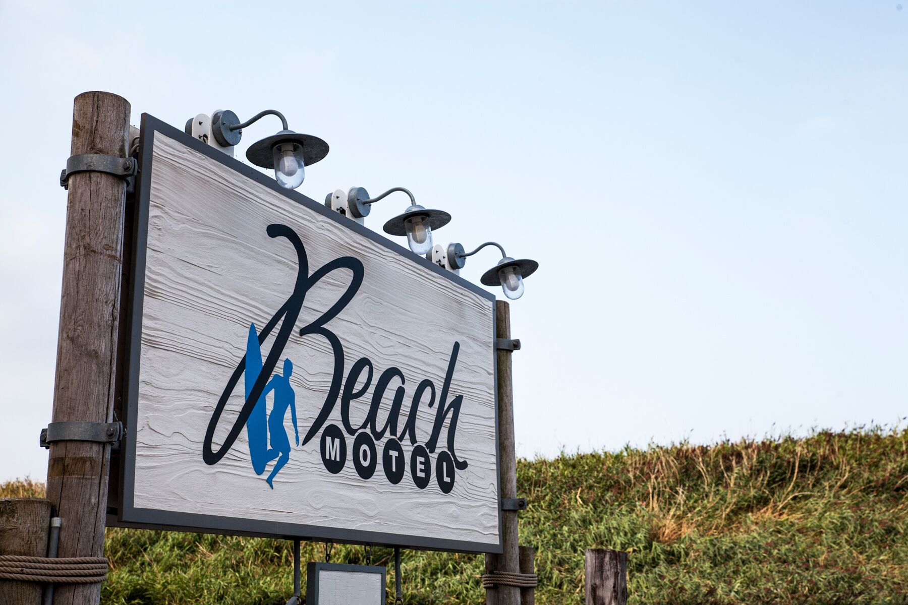 Une enseigne en bois portant l’inscription « Beach Motel » et représentant en silhouette bleue une personne.