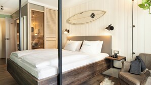 Un dormitorio moderno con una cama de madera, una mesita de noche con una cámara y una tabla de surf en la pared.