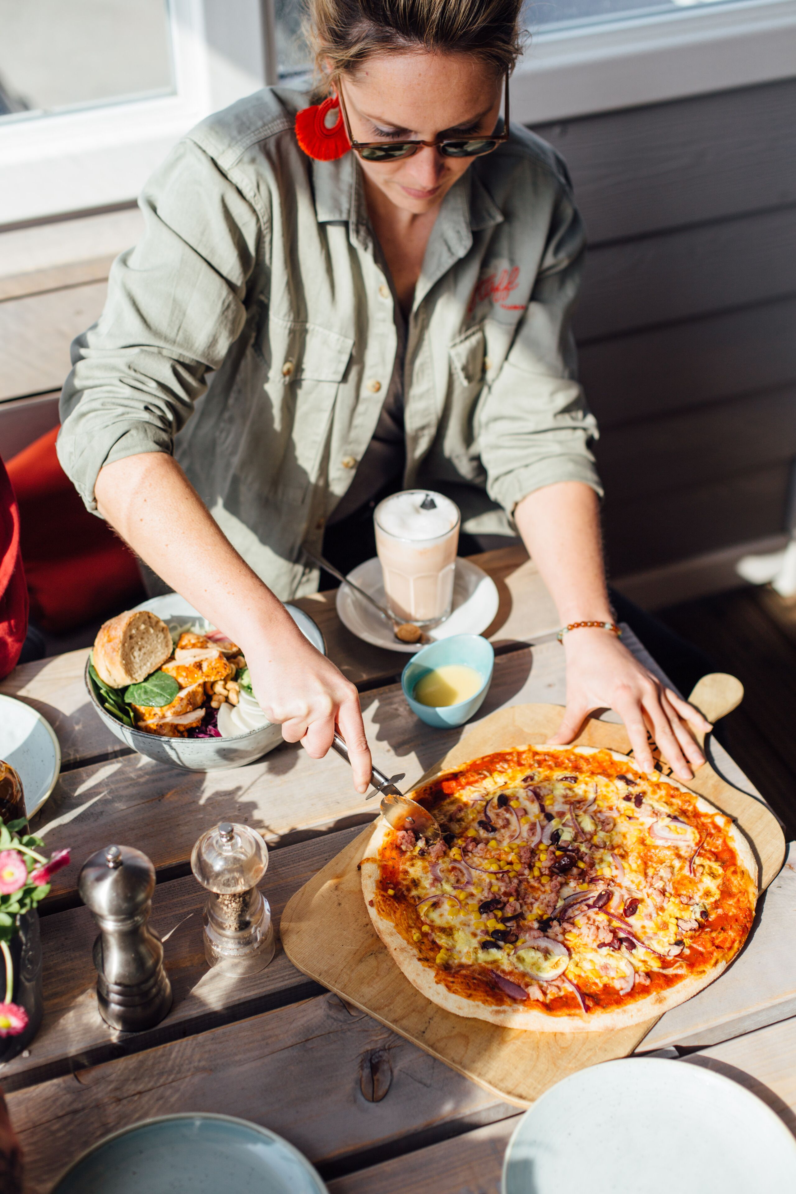 Eine Person sitzt an einem Holztisch mit einer Pizza, einer Salatschüssel und einer Tasse Kaffee.