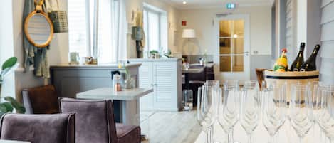 Un espace repas avec une longue table dressée, des verres à vin disposés dessus, un coin bar avec des bouteilles, et une cuisine en arrière-plan.