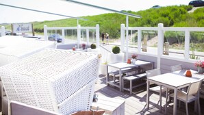 Terraza con mobiliario de mimbre blanco y una mesa con sillas, con vista a una playa que muestra un letrero que dice "Beach".