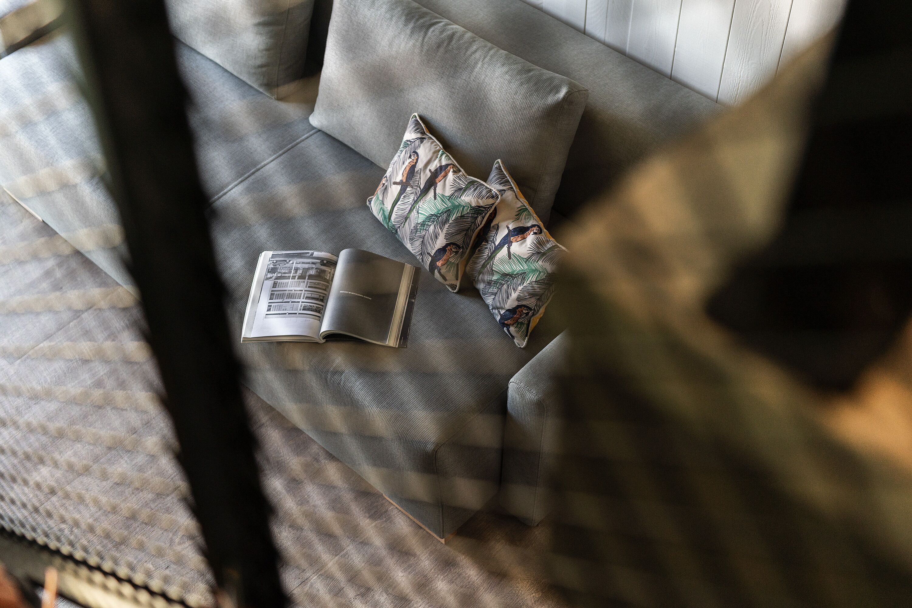 Un sofà gris amb coixins estampats i un llibre a sobre.