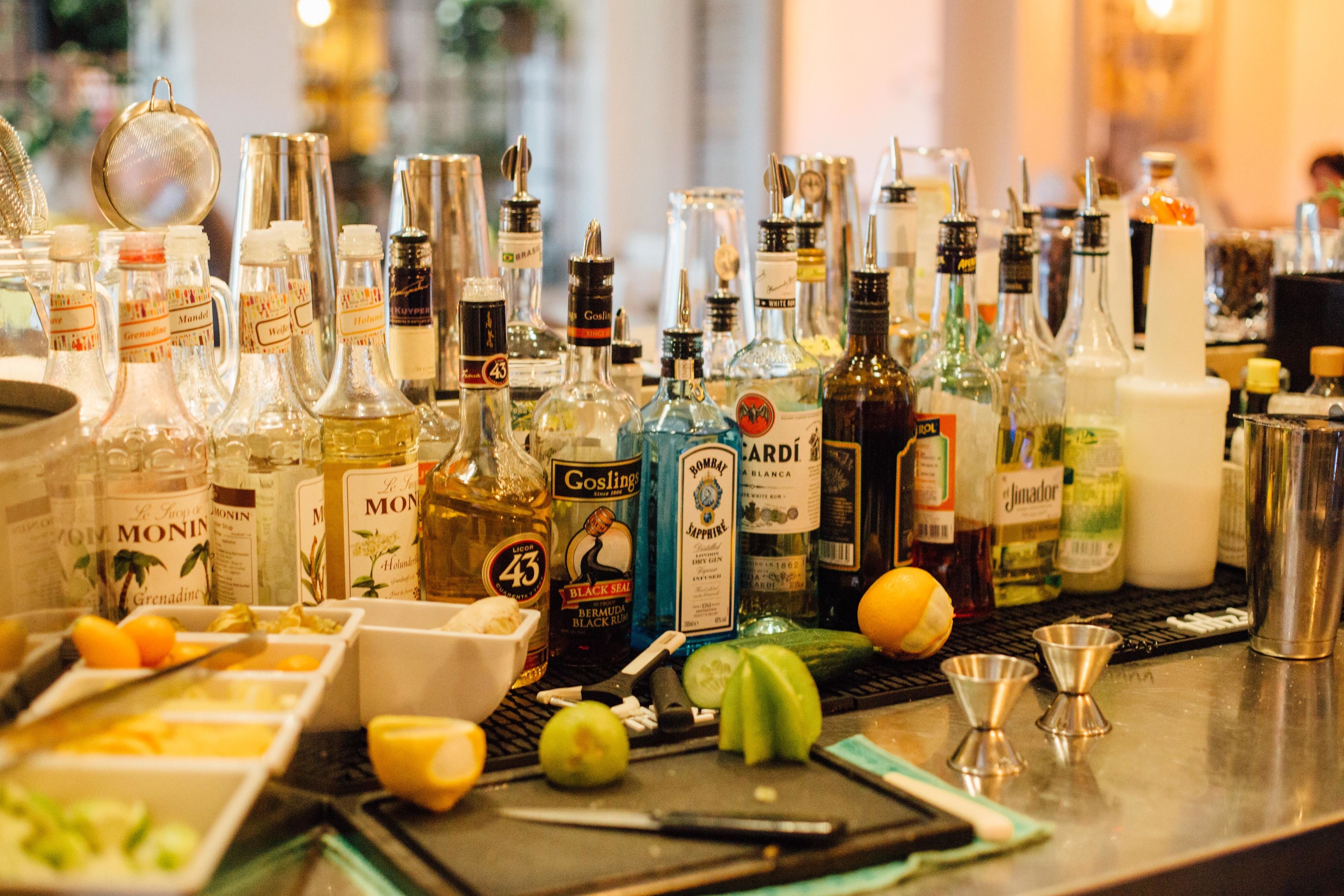 A bar area with various bottles of alcohol, a strainer, lemons, and a knife on the counter.
