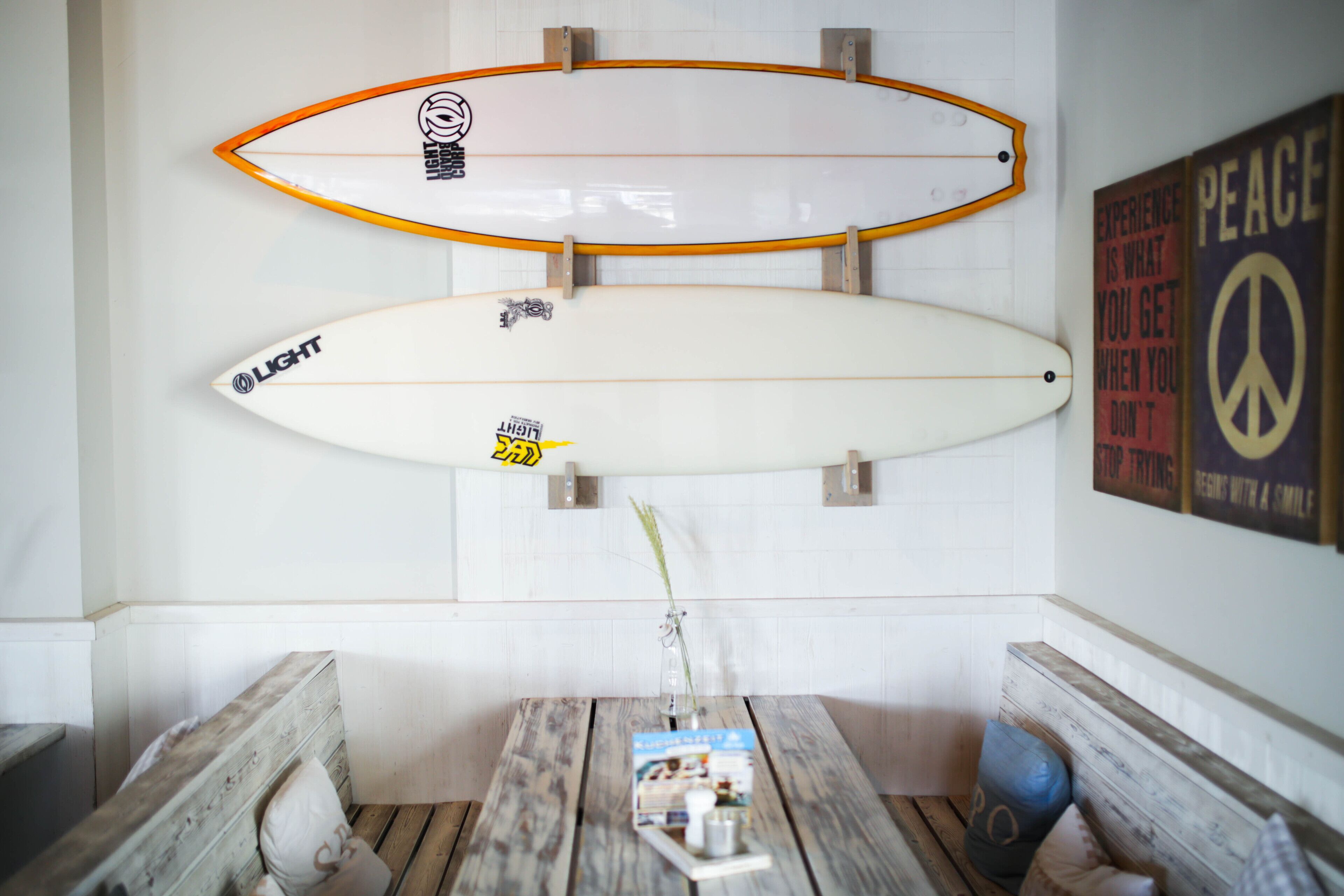 Two surfboards mounted on a wall, a wooden bench, a table with a magazine, and a peace sign poster.