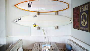 Two surfboards mounted on a wall, a wooden bench, a table with a magazine, and a peace sign poster.