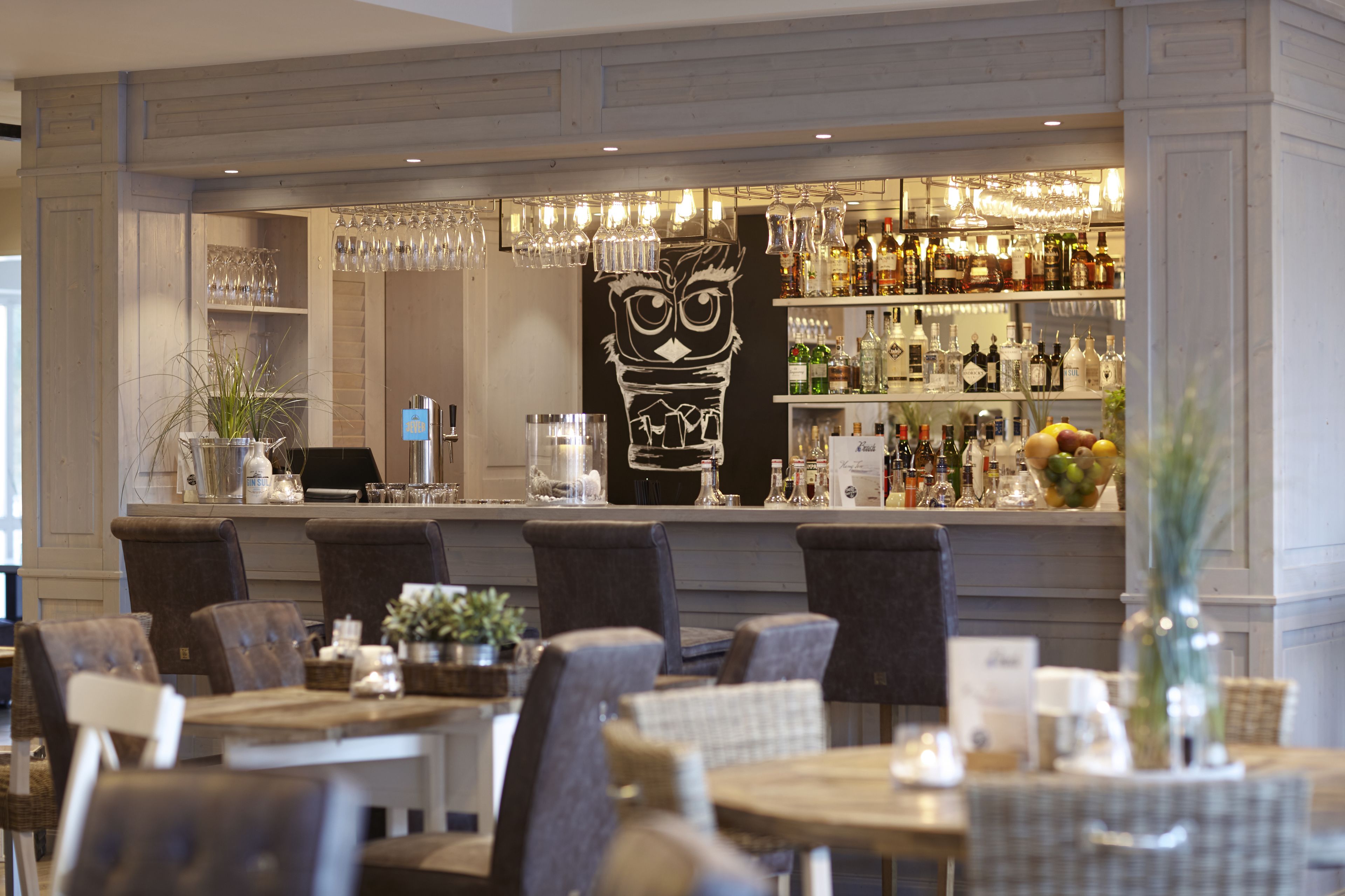 A bar area with a large owl sculpture, bar shelves stocked with bottles, and a seating area with chairs and tables.