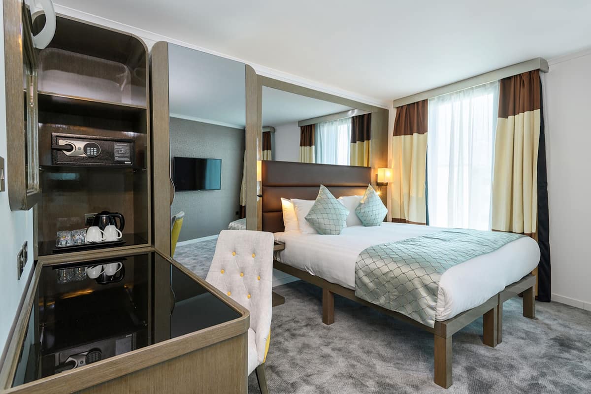 A hotel room with a bed, bedside table, and a built-in desk with a mirror.
